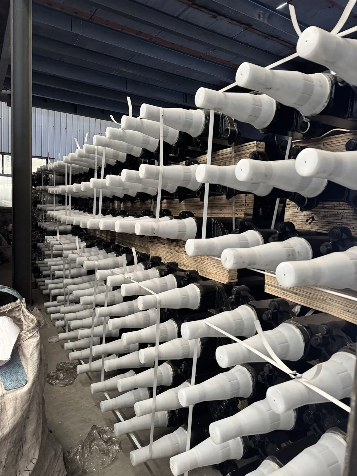 Trailer axle beams with protective end caps stacked in stock